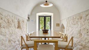 A dining room with a long wooden table and six chairs, set against textured stone walls. - LaCasa Apulia (Ceglie Messapica)
