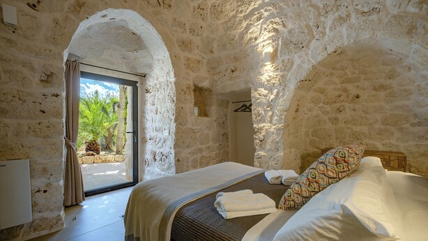 A bedroom with a stone wall, a bed with a patterned pillow, and a door leading to a balcony. - LaCasa Apulia (Ceglie Messapica)