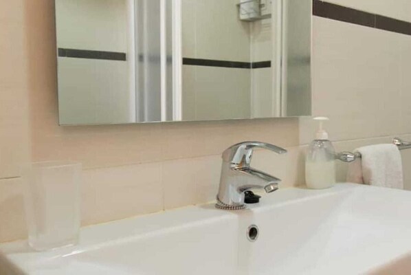 Une salle de bain avec un lavabo blanc, un miroir, un robinet, un distributeur de savon et un verre.