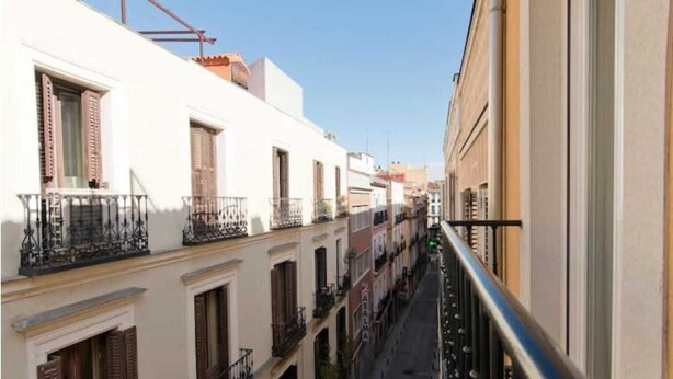 Une rue étroite en milieu urbain, bordée d’immeubles dotés de balcons et de volets.