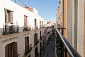 Une rue étroite en milieu urbain, bordée d’immeubles dotés de balcons et de volets.