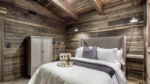 A bedroom with a wooden ceiling, a bed with white bedding, a bedside table with a tray, and a wardrobe. - Pet Friendly Home!- Mayfly Meadow | Cozy Cabin | World-Class Fishing | Fire Pit | BBQ (Island Park)