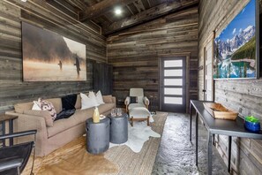 A rustic interior with a wooden wall, a sofa, a chair, a table, and two paintings.