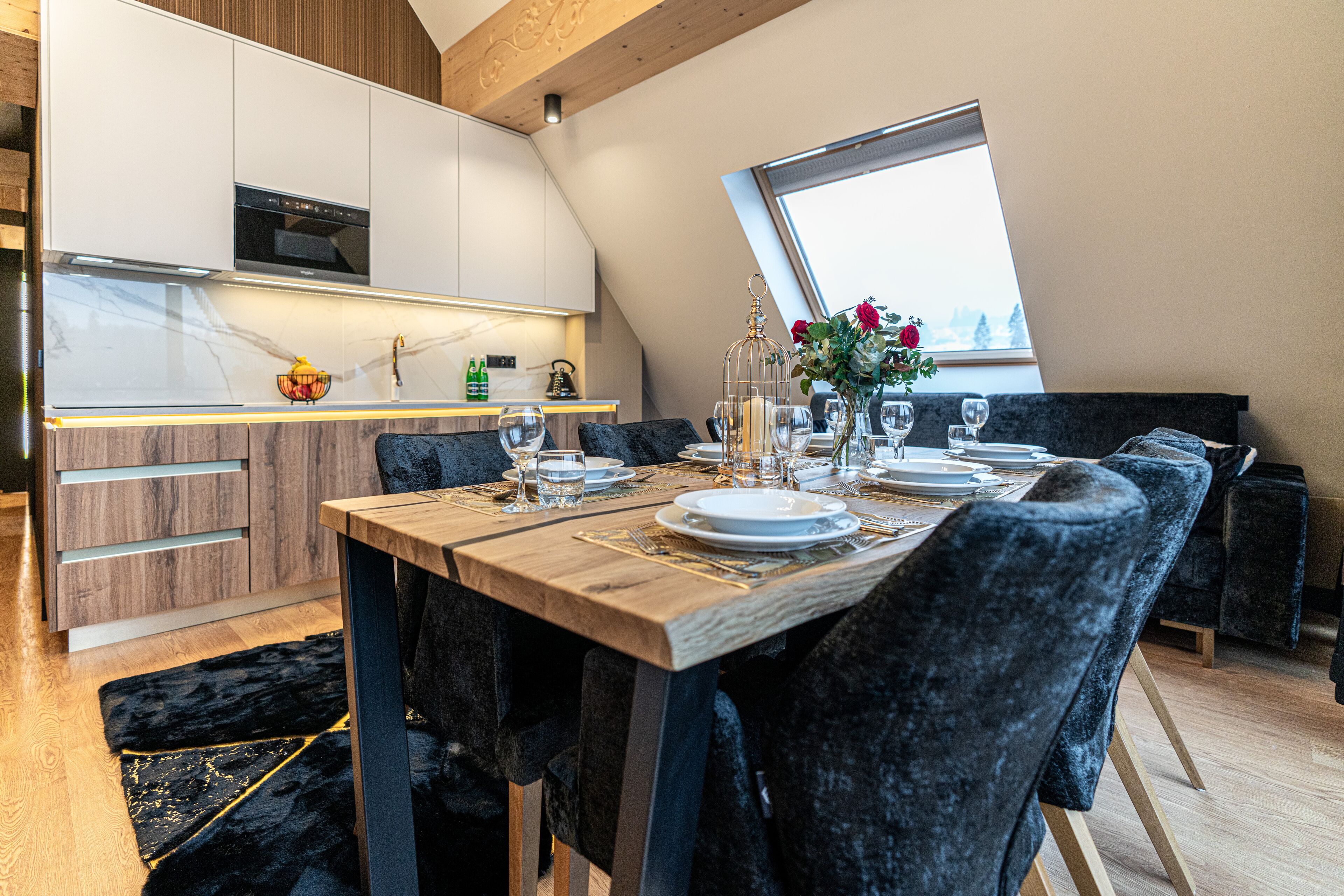 Ein zeitgemäßer Essbereich mit einem Holztisch, gedecktem für vier Personen, dunklen Polsterstühlen und Blick auf die Stadt durch ein großes Fenster.