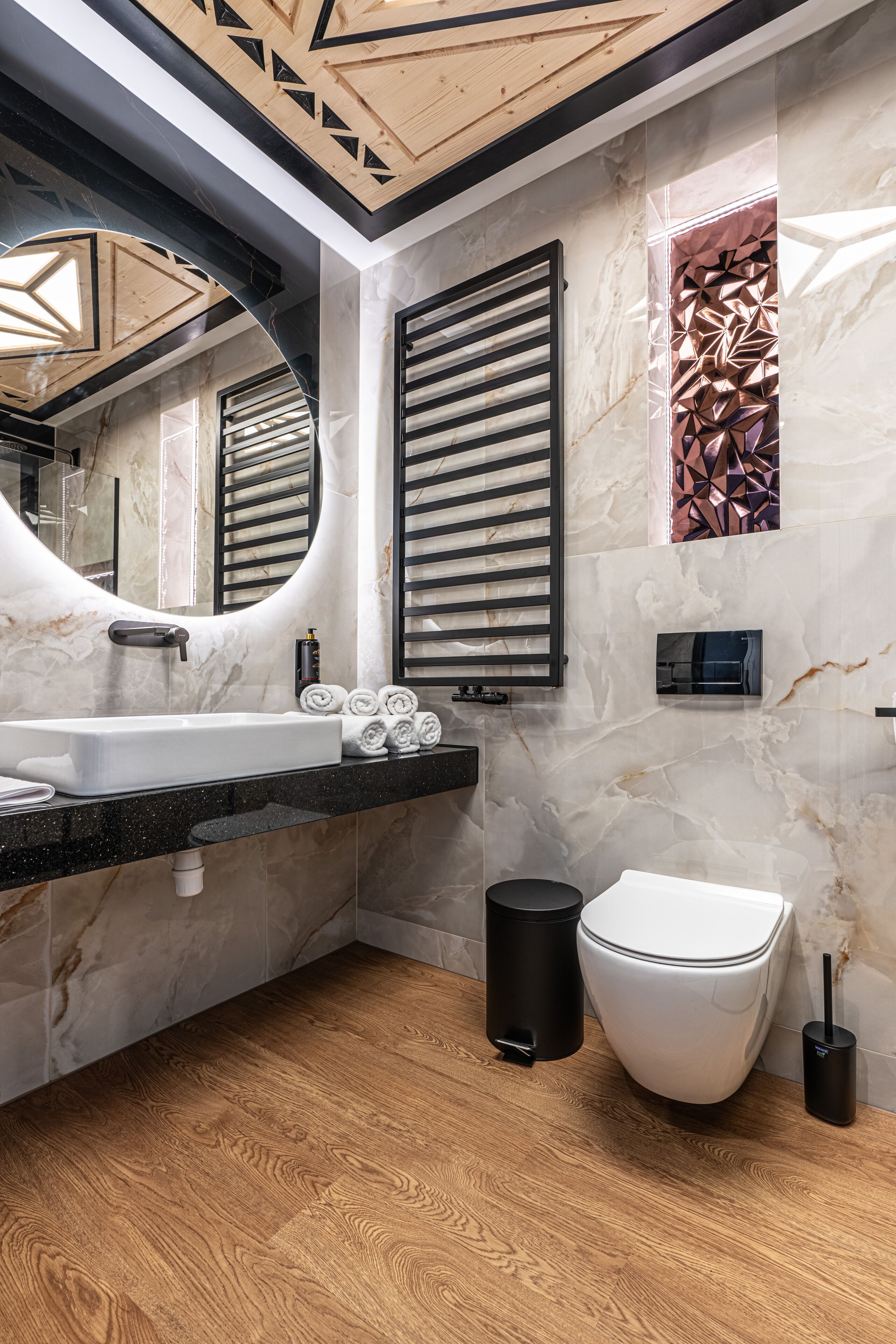 Ein modernes Badezimmer mit Marmorwaschbecken, Wänden mit Schwarz-Weiß-Fliesen, Holzboden und Toilette mit schwarzem Mülleimer.