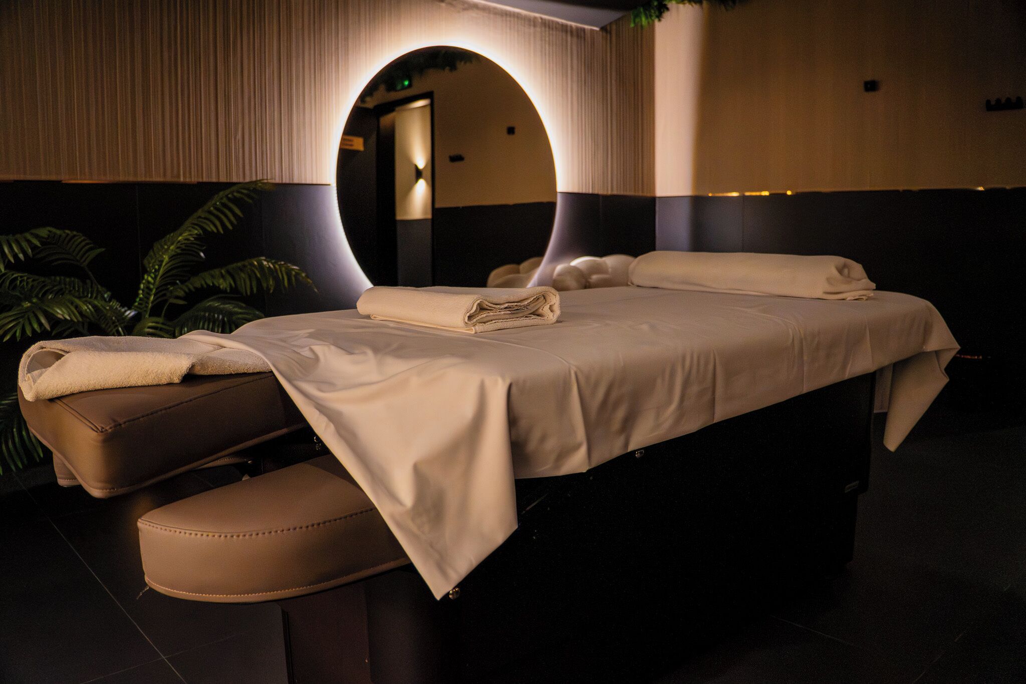 A spa room with a bed, a massage table, and a large mirror.