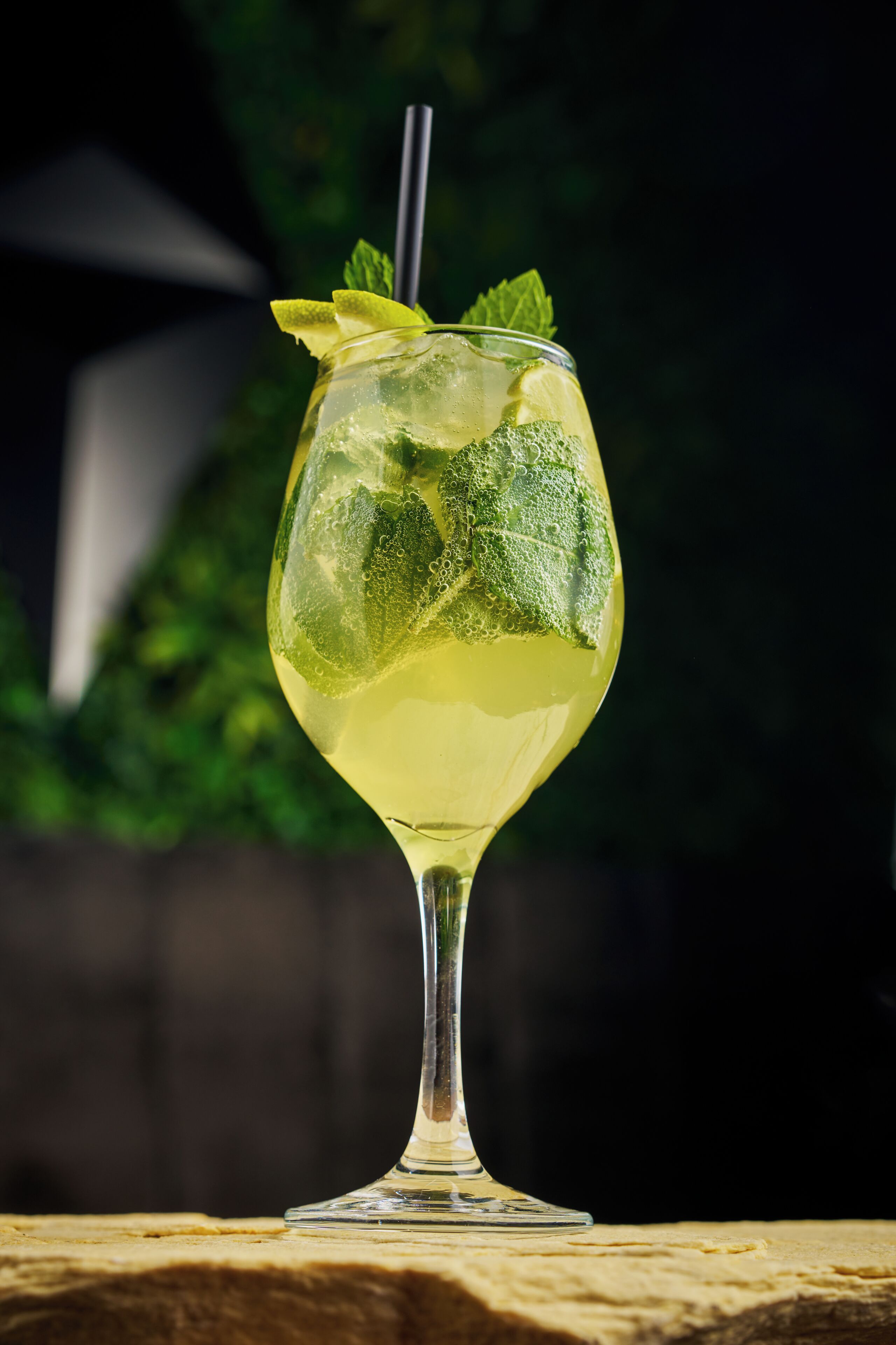 A clear glass with a straw, garnished with mint leaves and lime slices, placed on a wooden surface.