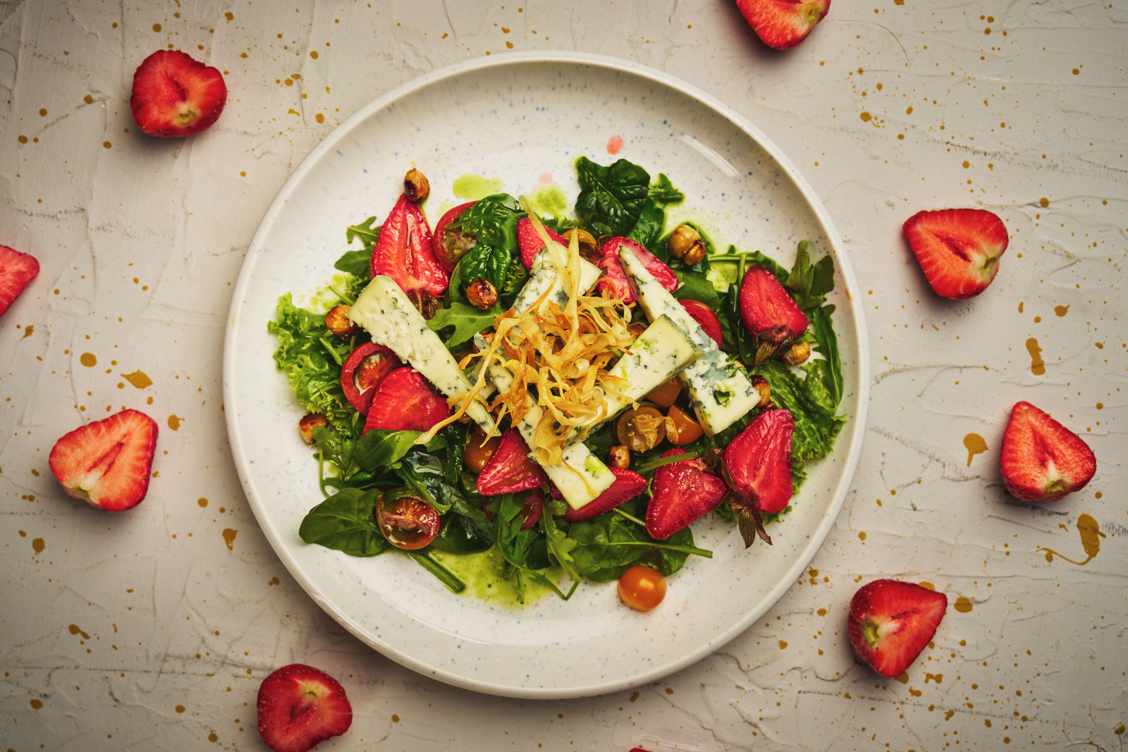 A plate of salad with strawberries, nuts, and cheese on a textured surface.