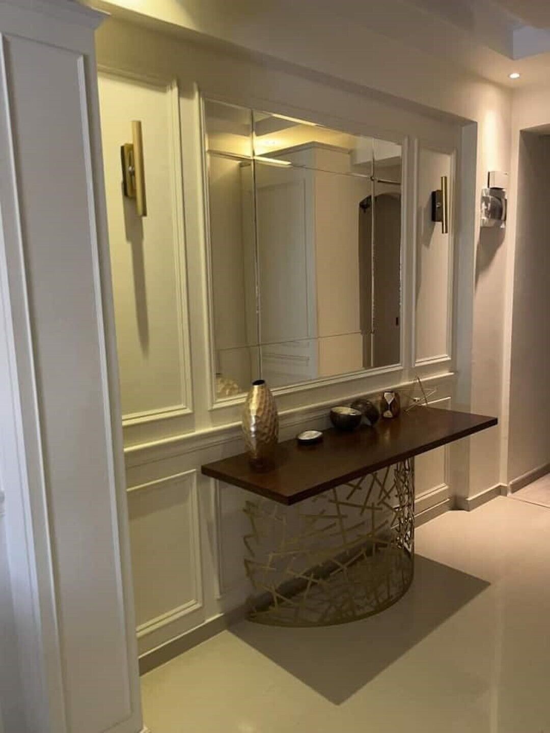 A modern hallway with a large mirror, a dark wooden console table, and a decorative vase.