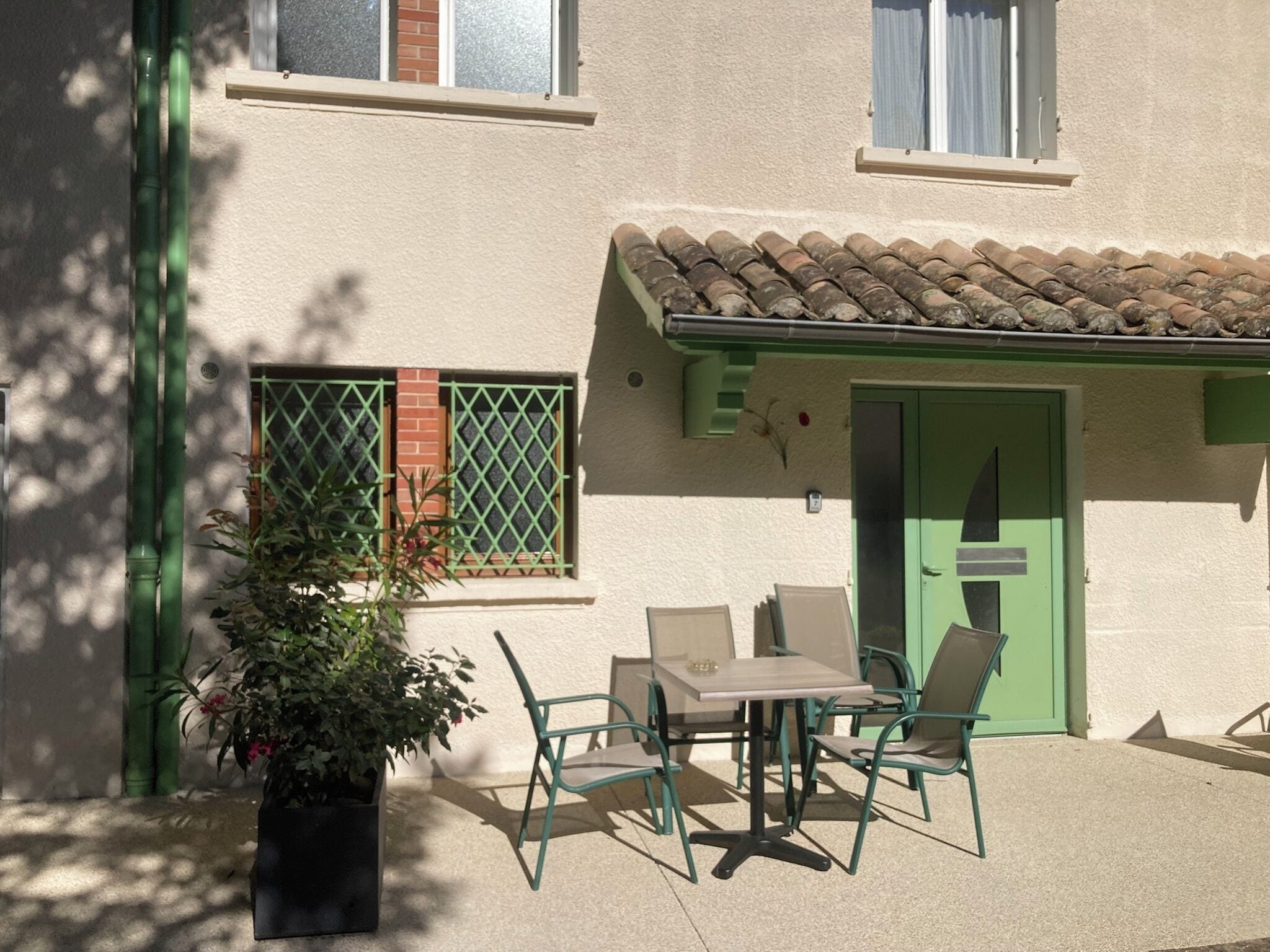 A building with a tiled roof, a green door, and a patio with a table and chairs.