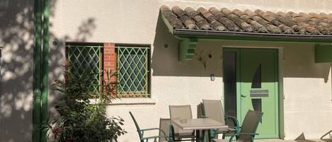 A building with a tiled roof, a green door, and a patio with a table and chairs.