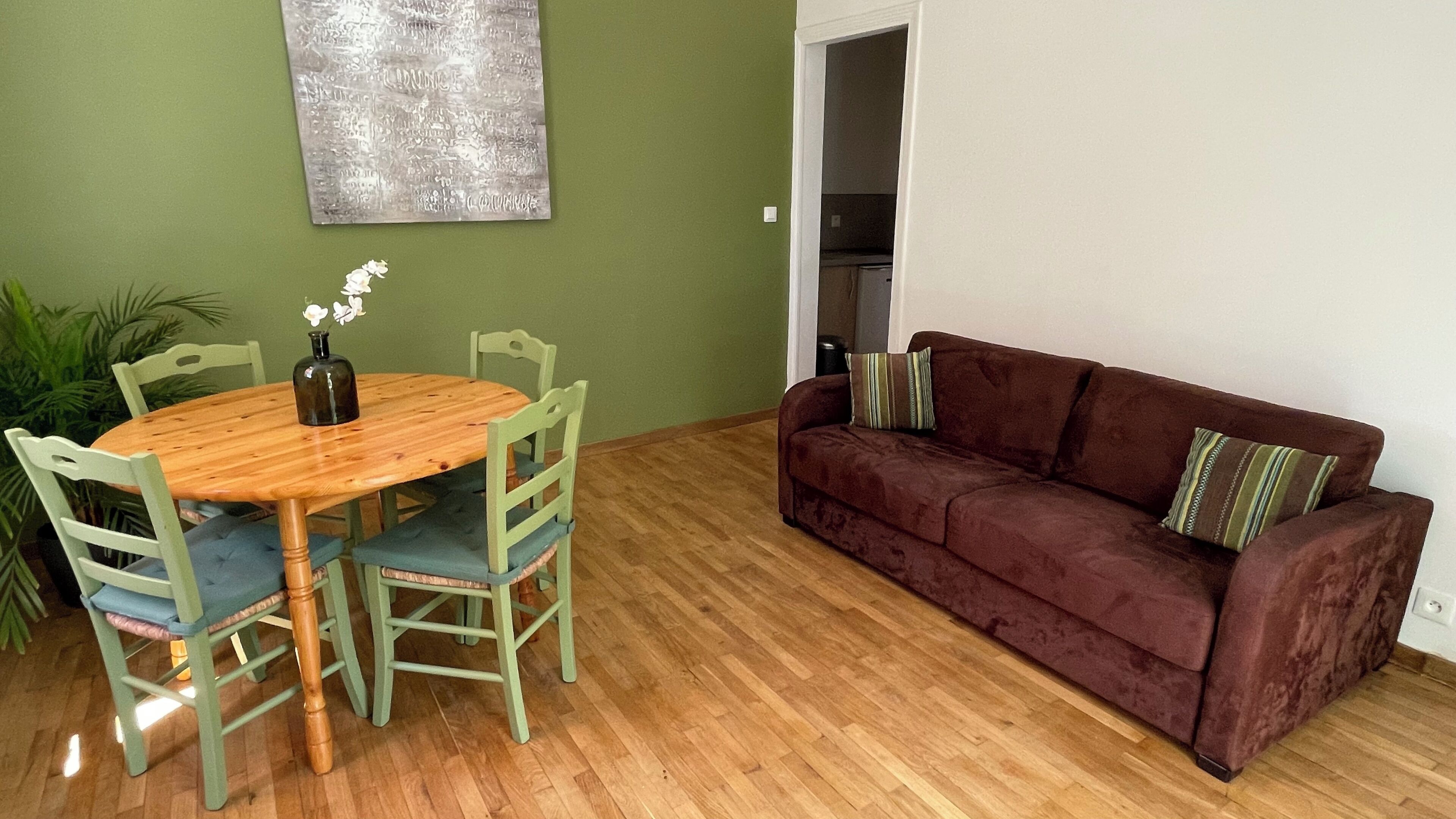 Un comedor con una mesa y sillas de madera, un sofá marrón y una pared verde.