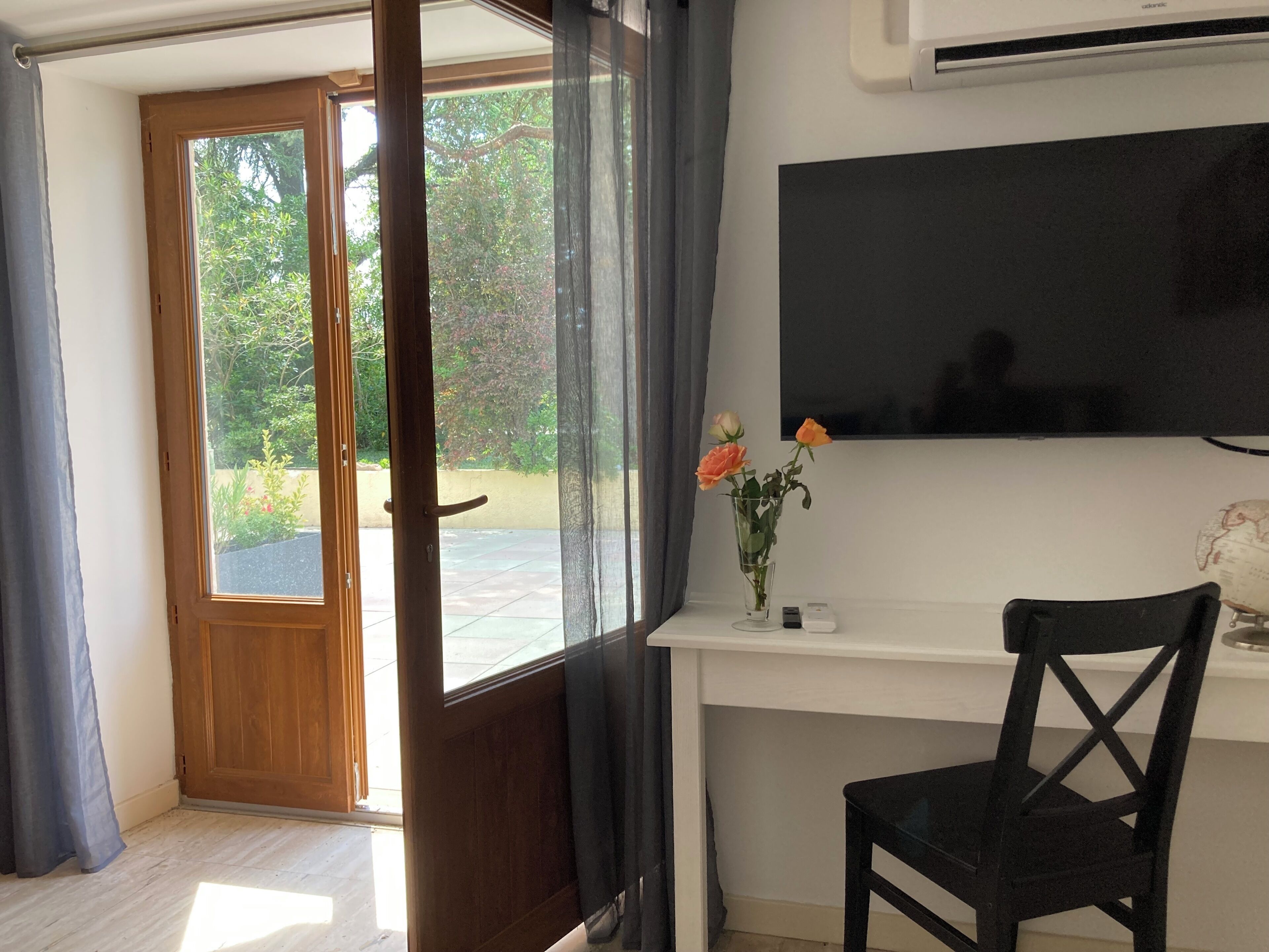 Habitación con puerta de madera que da a un espacio exterior, un escritorio con silla, un jarrón con flores y un globo terráqueo fijado a la pared.