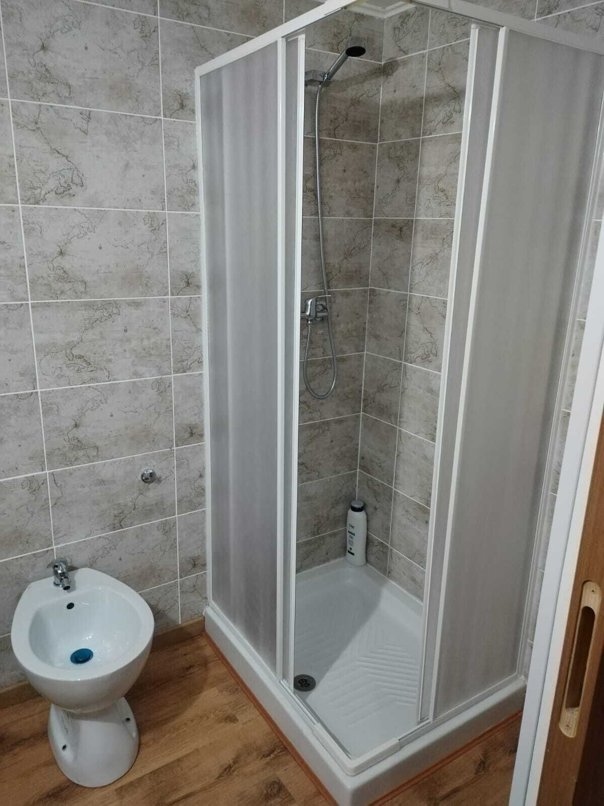 Une salle de bain avec un espace douche, un lavabo sur colonne blanc et un plancher en bois.