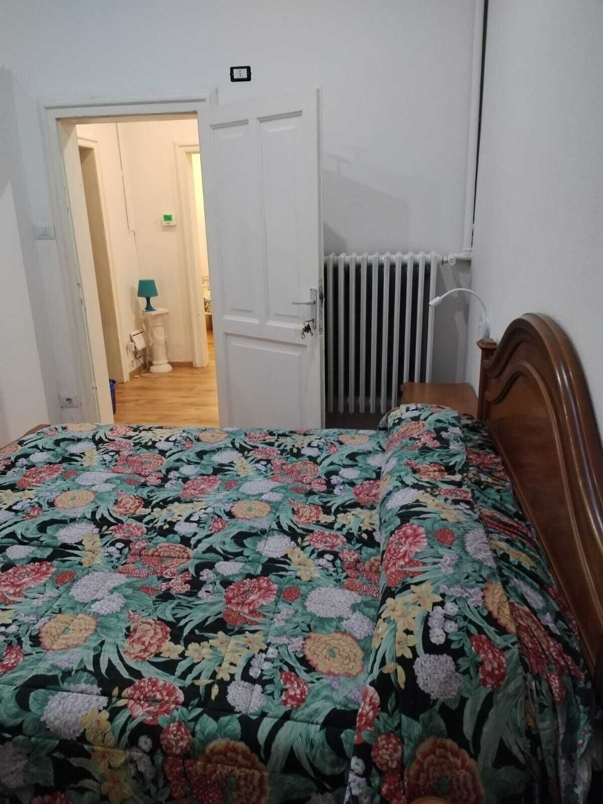 A bedroom with a floral bedspread, a radiator, and a door leading to another room.