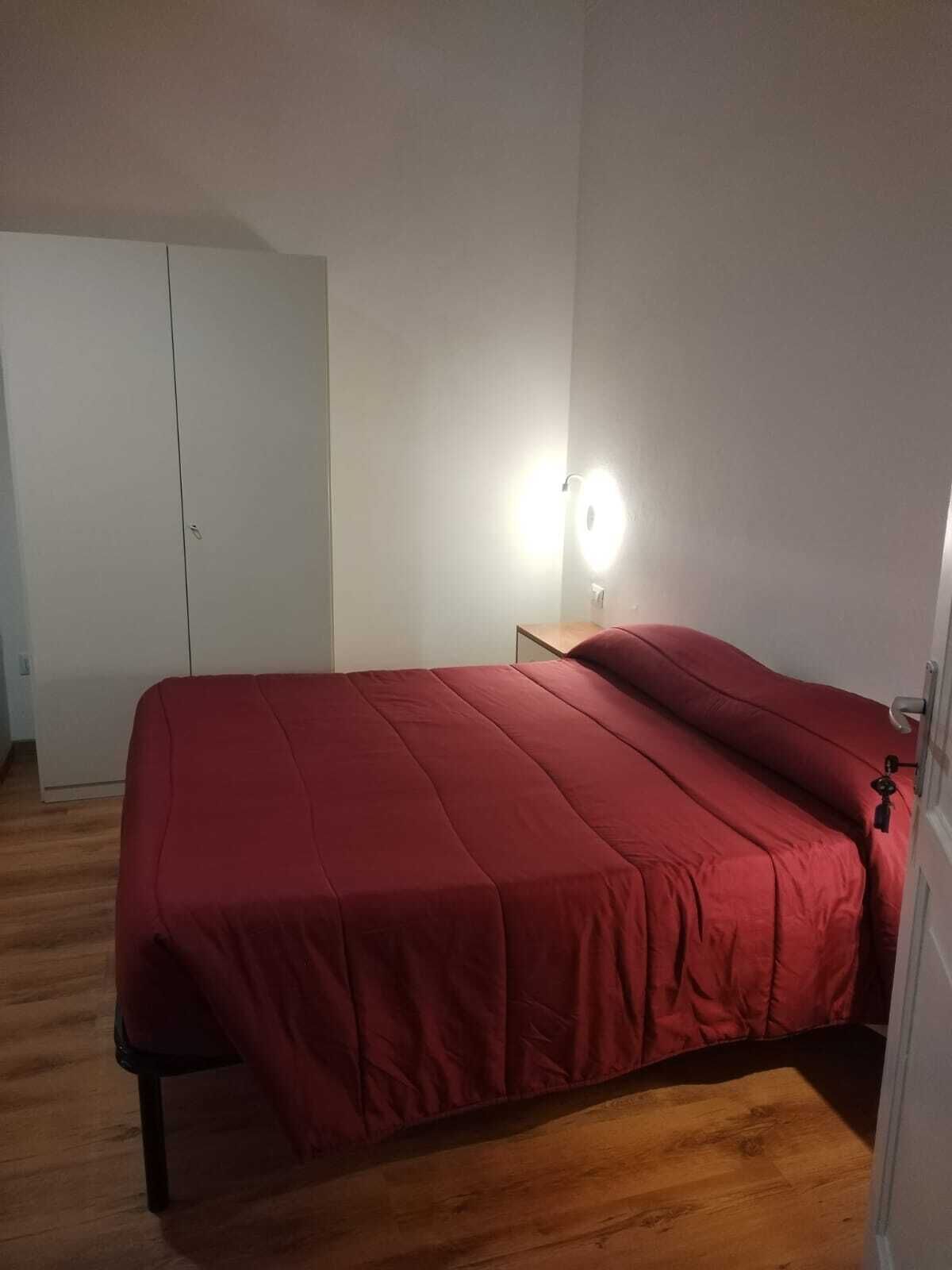 Un dormitorio con cama, mesita de noche, armario y una puerta.