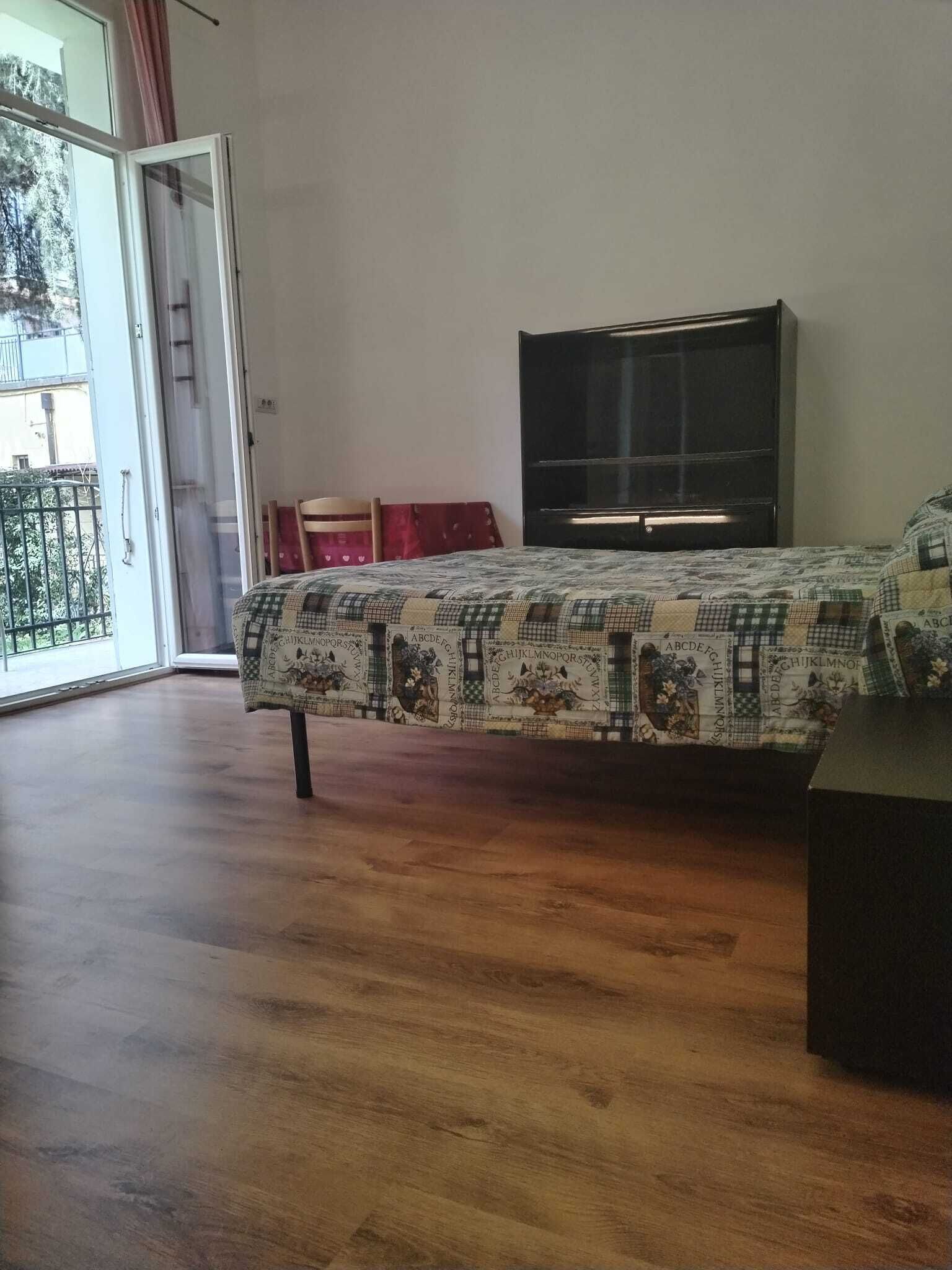 A bedroom with a bed, a TV, and a sliding glass door to a balcony.