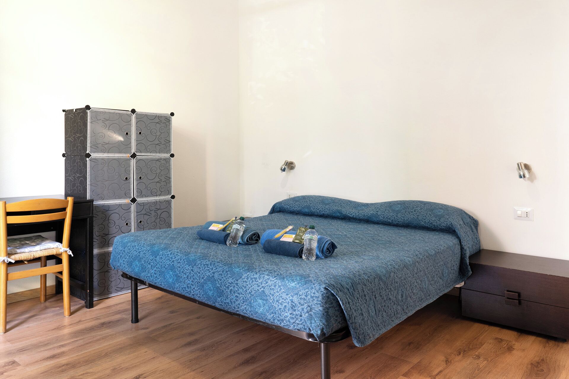A small, neatly arranged bedroom with a bed, a chair, a wardrobe, and a desk.