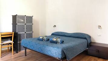 A small, neatly arranged bedroom with a bed, a chair, a wardrobe, and a desk.