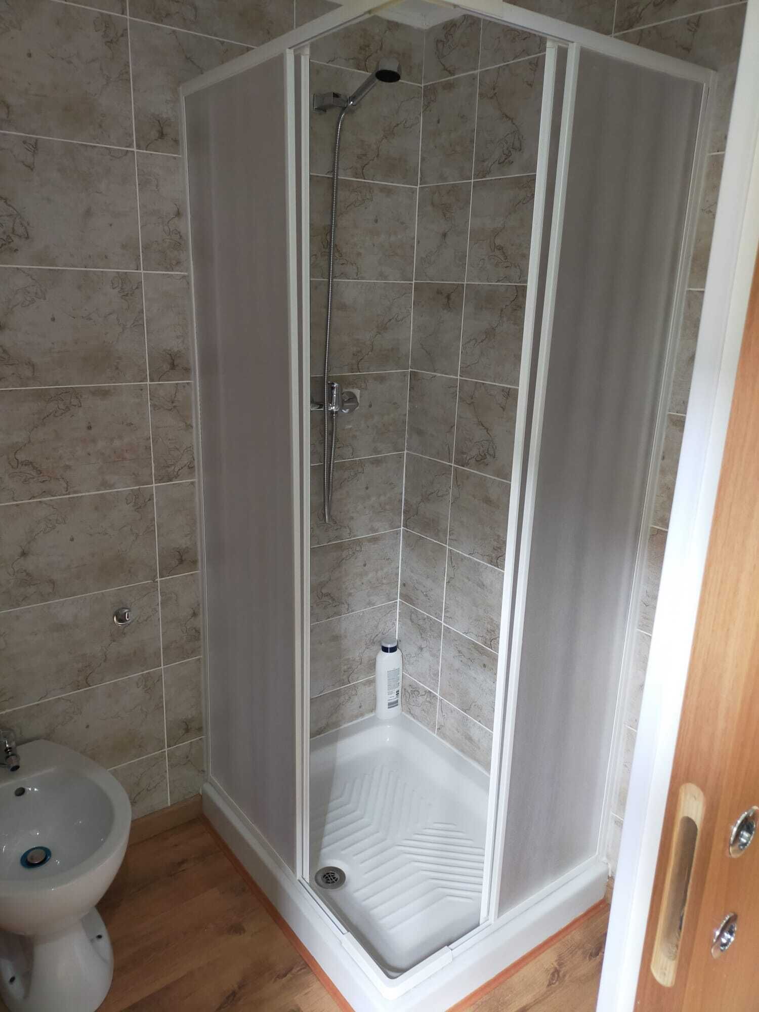 A corner shower with a glass door, a white pedestal sink, and a toilet.