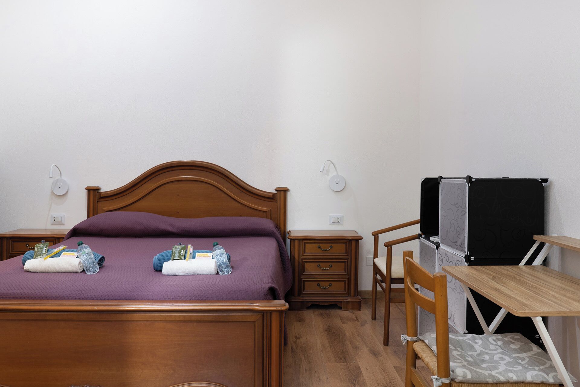 A bedroom with a wooden bed, a nightstand, a desk with a chair, and a black radiator.