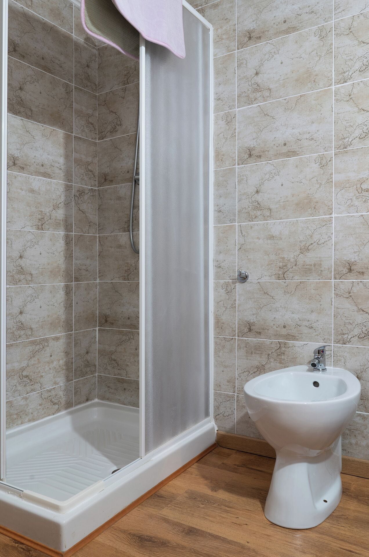 A shower enclosure with a glass door, a white sink, and a wooden floor.