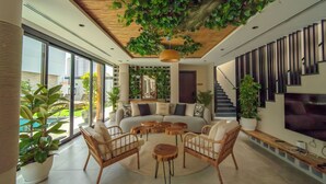 A modern living room with a sofa, wicker chairs, and round wooden tables. - Nas House Private Villas (Dubai)