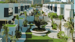 A modern hotel complex with a central courtyard, surrounded by white buildings with large windows and palm trees. - Nas House Private Villas (Dubai)