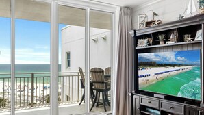 Un balcon avec vue sur la plage, une télévision et une table en bois.