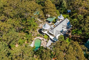 An aerial view of a large estate with multiple buildings, a swimming pool, and dense surrounding vegetation.