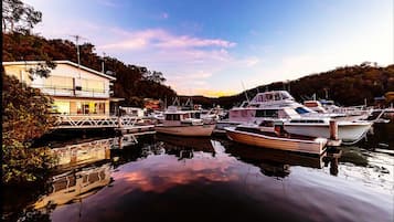 A marina with several boats docked, a building with a balcony, and a calm water body reflecting the sky.