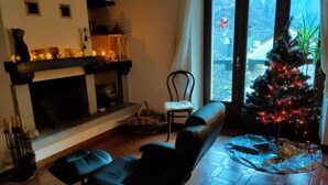 Un salon chaleureux avec une cheminée, un fauteuil inclinable, un sapin de Noël et une vue magnifique par une grande fenêtre.