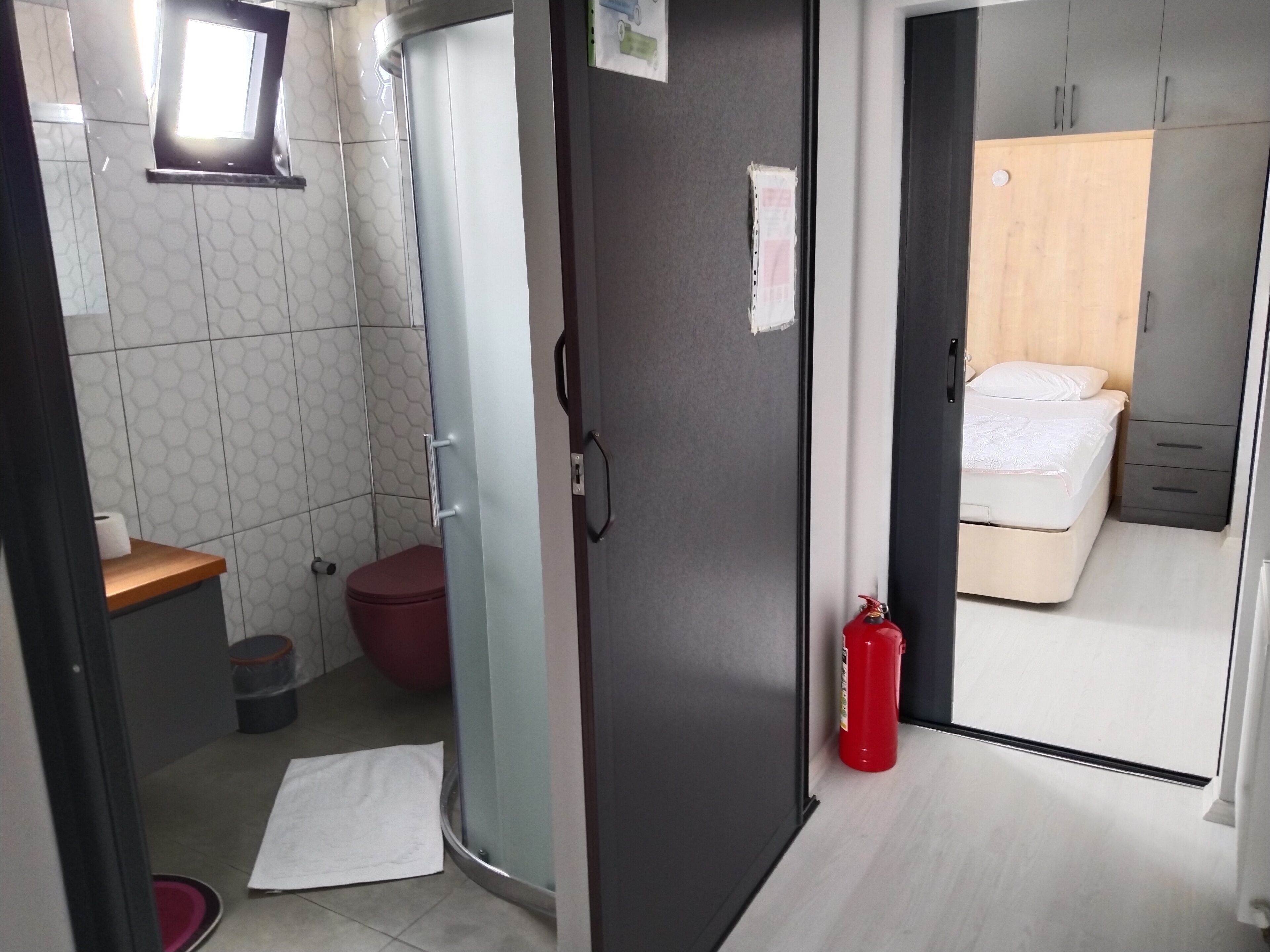 A compact room with a shower, toilet, and a bed.