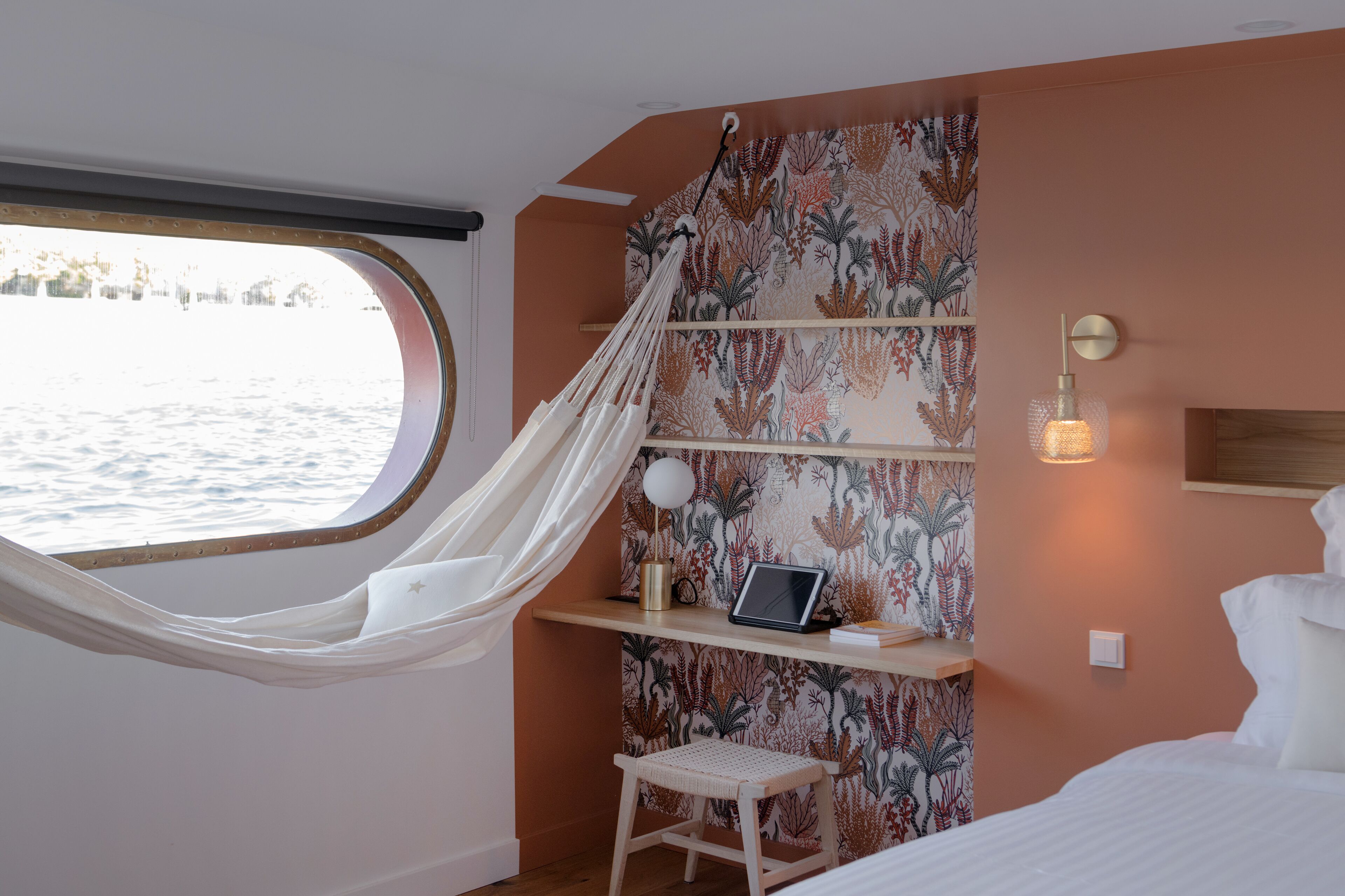 A room with a hammock, a laptop on a shelf, and a view of the water outside.