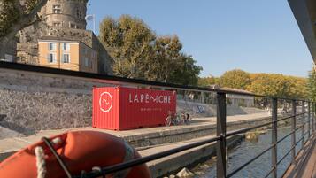 A red shipping container labeled "LAPEMCHE" on a dock with bicycles and a stone wall in the background.