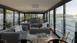 A modern, open-plan living area with a large window overlooking a body of water, furnished with sofas and a coffee table. - LA PENICHE - Bed And Bicycle - Tournon (Tournon-sur-Rhone)