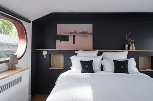 Un dormitorio moderno con una cama grande, una pintura de paisaje urbano y vista a un cuerpo de agua a través de una ventana.