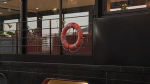 A boat with a lifebuoy, a small seating area with cushions, and a window with a view of the outside. - LA PENICHE - Bed And Bicycle - Tournon (Tournon-sur-Rhone)