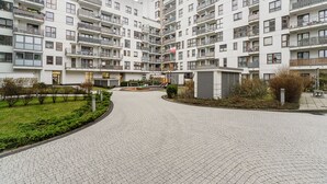 Un immeuble résidentiel à plusieurs étages, doté de balcons, d’une cour pavée et d’un petit jardin.