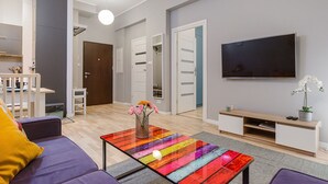 Un salon moderne avec un canapé, un tapis rayé aux couleurs vives, un téléviseur et une petite table sur laquelle est posé un vase de fleurs.