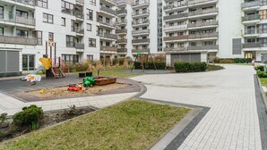 Un immeuble résidentiel moderne doté de nombreux balcons, d’une aire de jeux et d’un chemin piétonnier dallé.