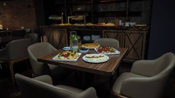 A restaurant setting with a wooden table set for four, featuring various dishes and a pizza.
