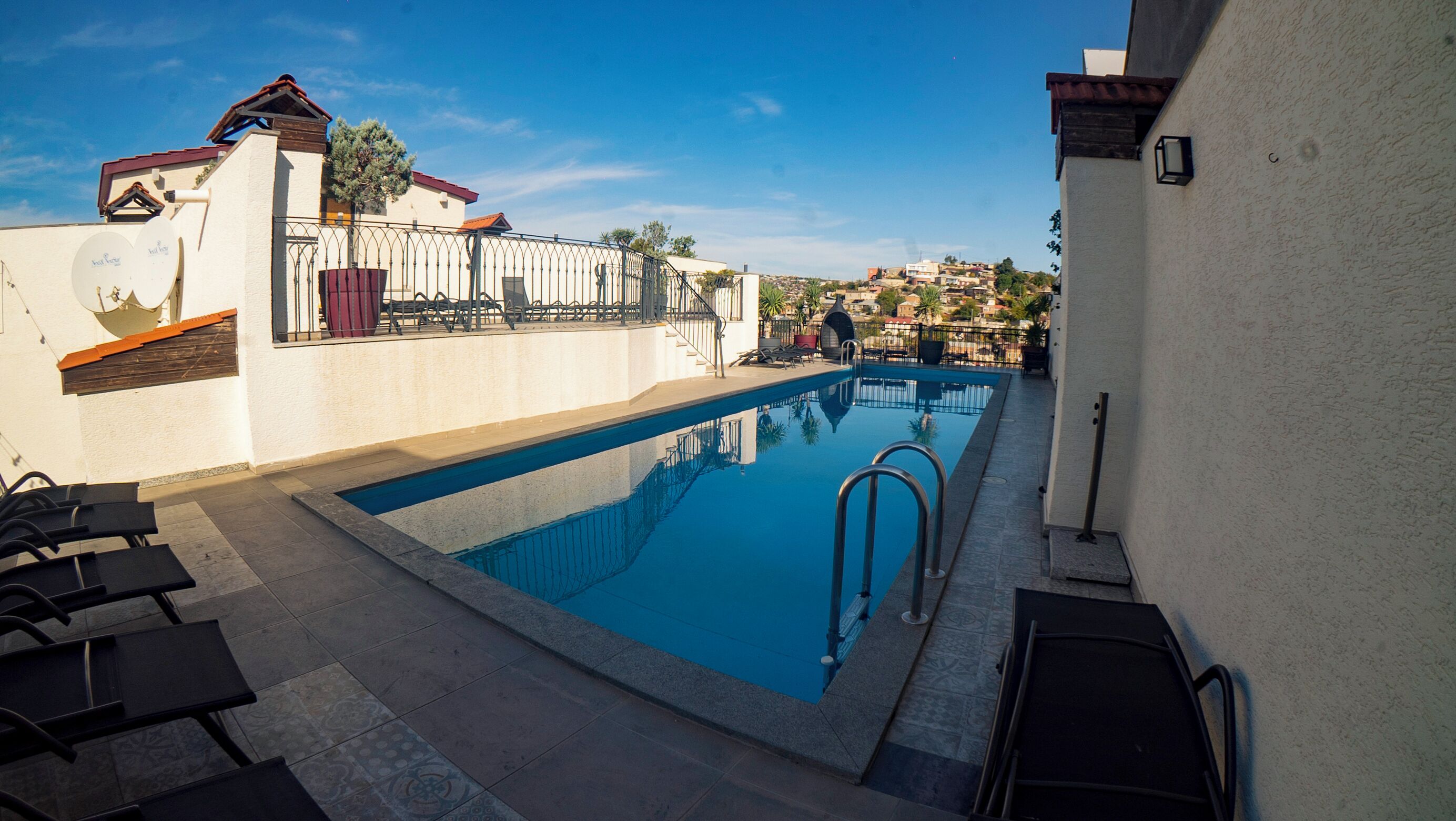 A swimming pool with a tiled deck, lounge chairs, and a view of a residential area in the background.