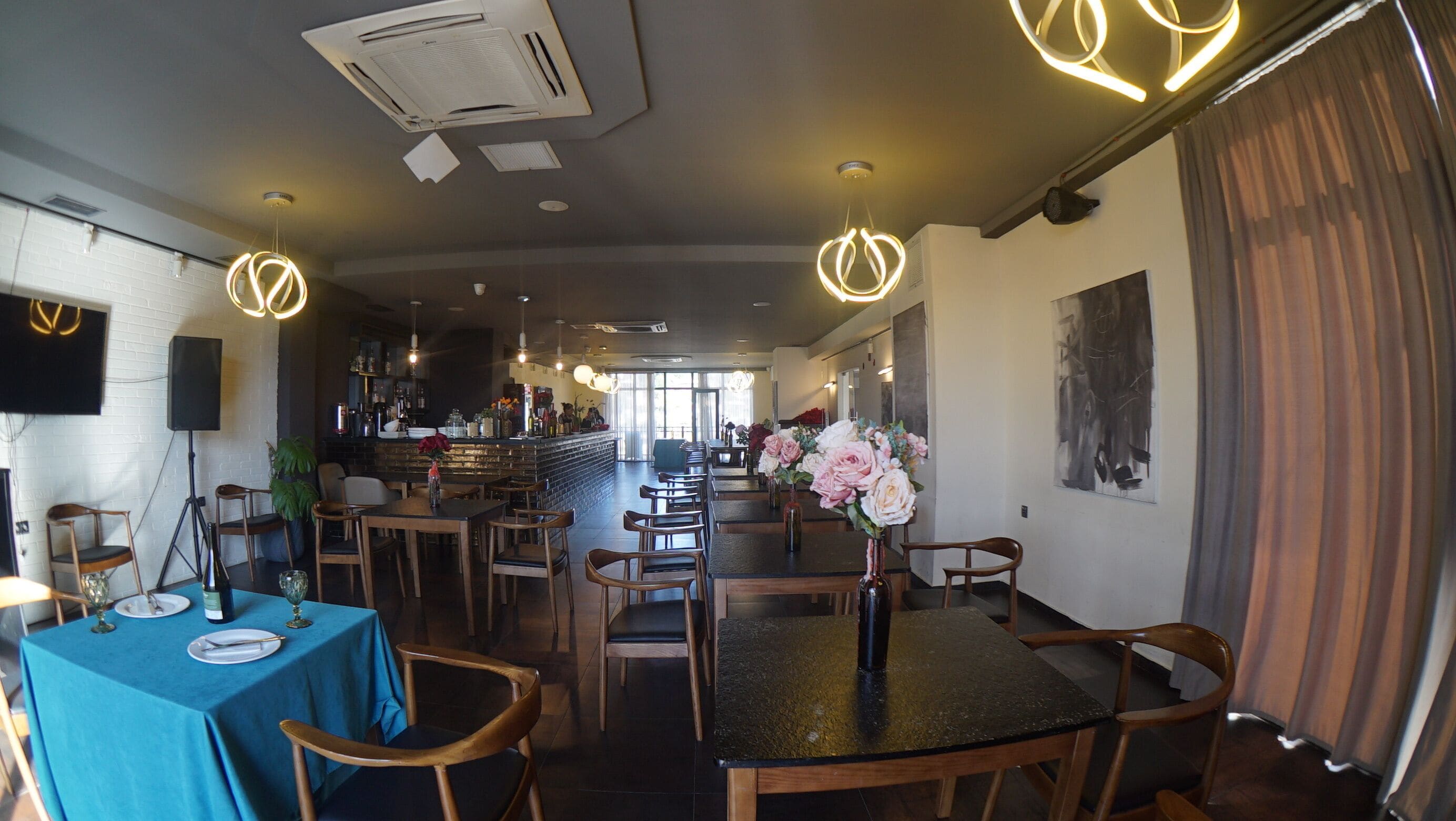 A restaurant with a bar area, wooden tables and chairs, and a large window providing natural light.