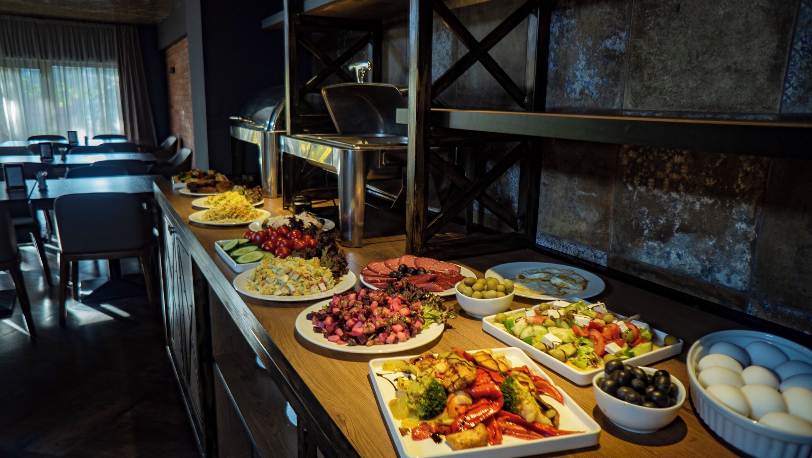 Ein reichhaltiges Buffet mit verschiedenen Speisen, eine Kaffeemaschine und im Hintergrund eine Sitzecke.