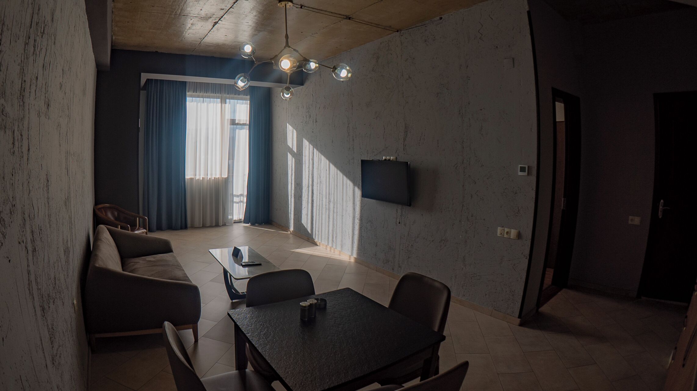 A modern living room with a sofa, a dining table, and a TV mounted on the wall.