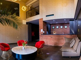 Un vestíbulo moderno con un mostrador de recepción, sillas rojas, una mesa redonda con un florero y una planta grande.