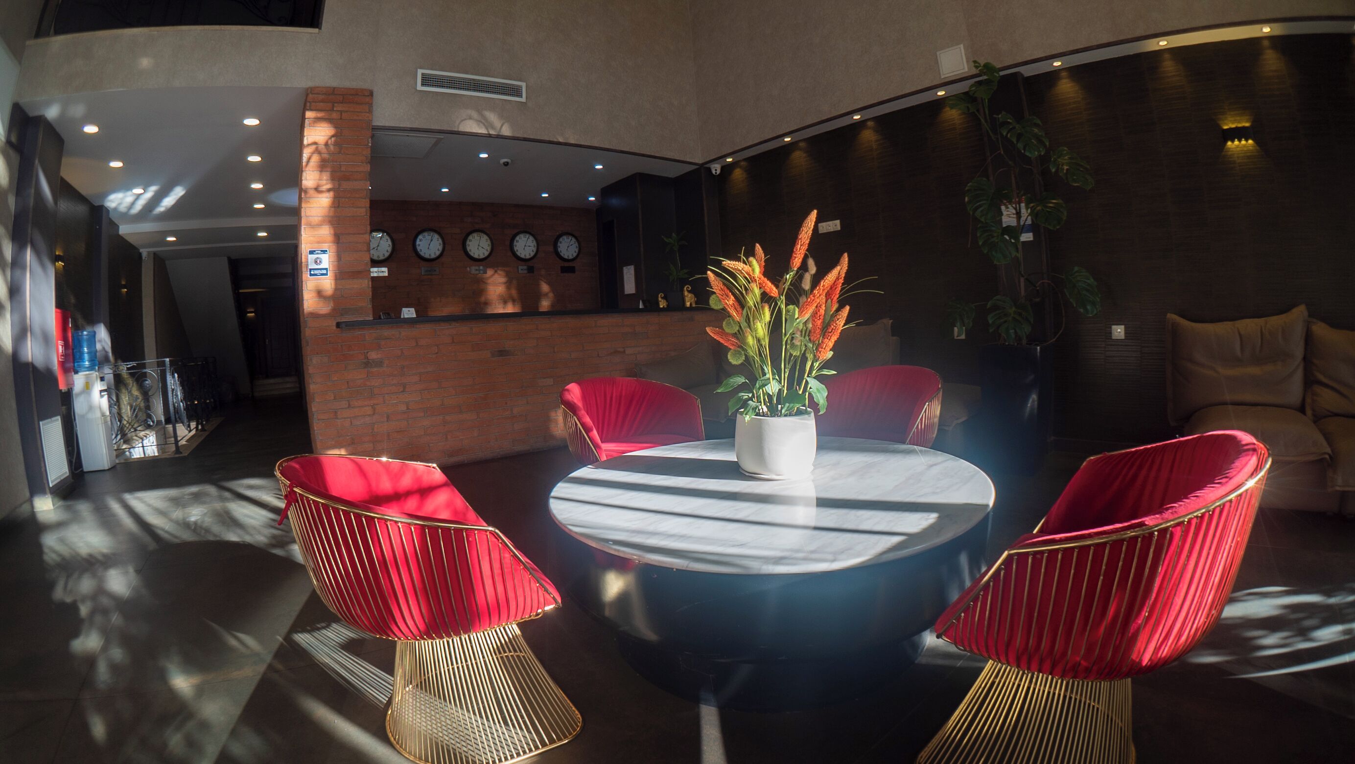 A modern dining area with a round table, red upholstered chairs, and a potted plant with orange flowers.
