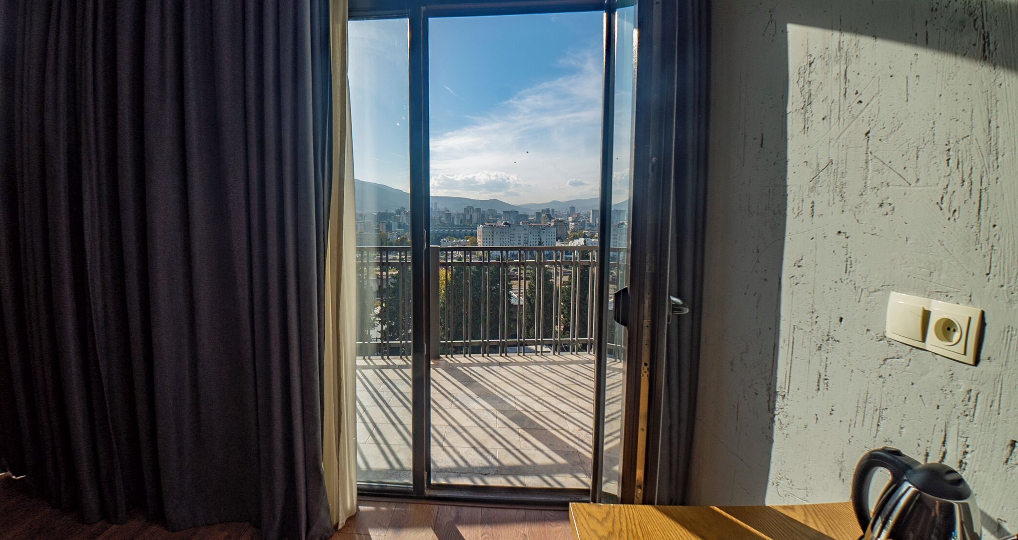 A room with a sliding glass door leading to a balcony with a city view.