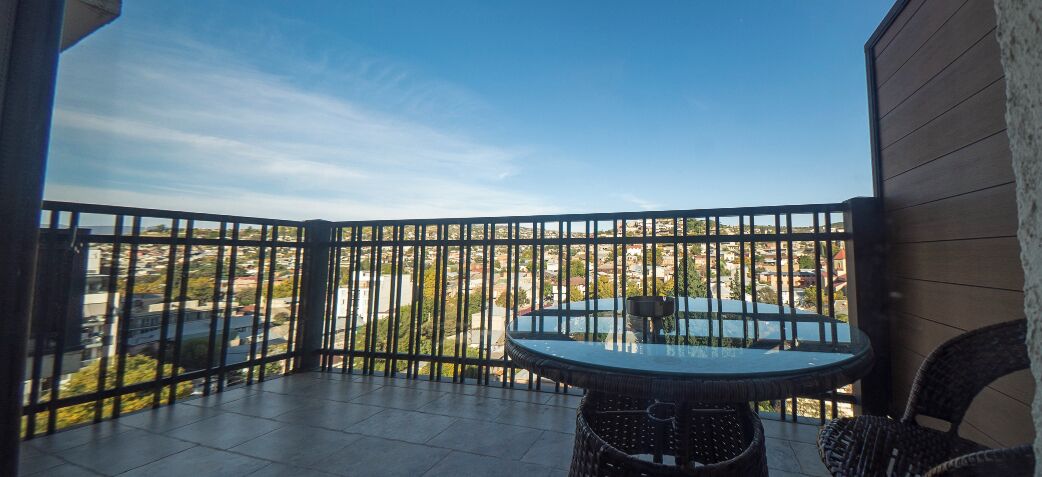 A balcony with a view of a cityscape, a round table, and wicker chairs.